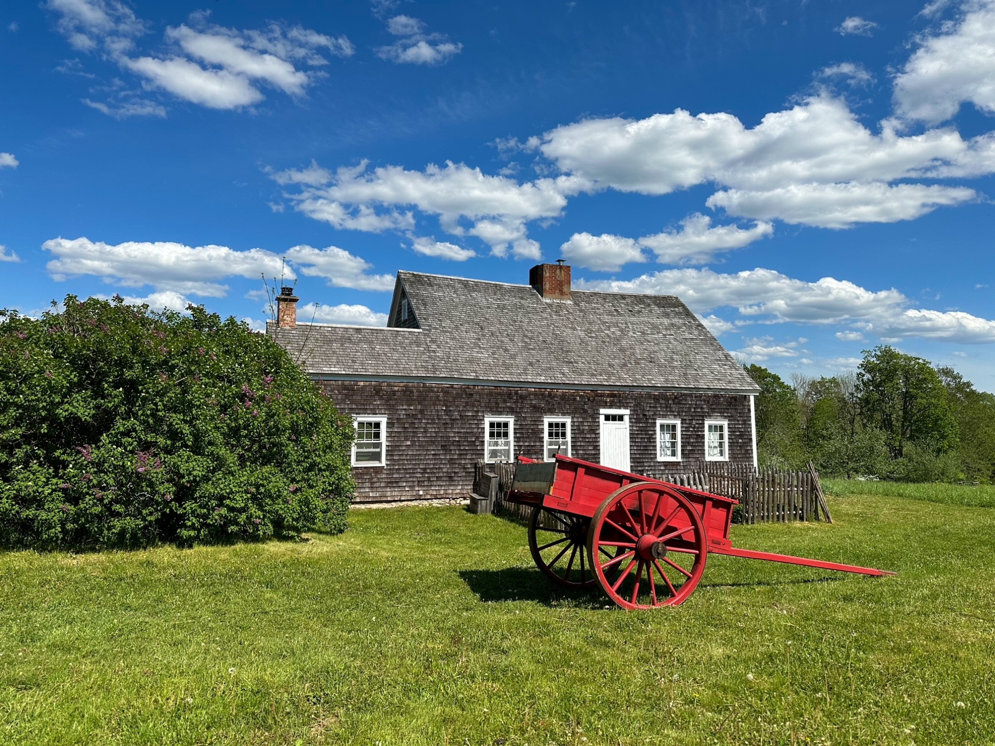 Ross bank cottage with a red wagon in front, blue sky.