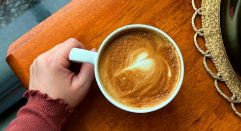 Down view of a wooden table and a hand holding a mug of coffee.