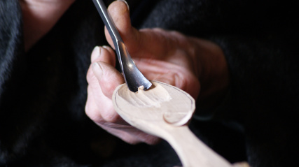 Close up of hands carving a wooden spoon with a spoon gouge.