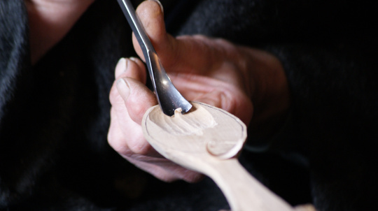 Close up of hands carving a wooden spoon with a spoon gouge.